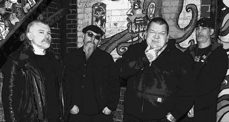 Sheer Terror band press photo, four members in dark clothing against a sticker-covered brick wall