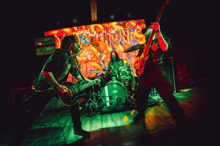 Dopethrone performing live, all three members on stage with fiery psychedelic backdrop at small venue