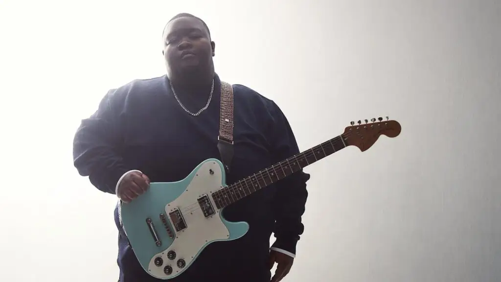 Christone Kingfish Ingram holding his signature seafoam Fender Telecaster, low-angle press photo