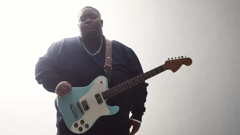 Christone Kingfish Ingram holding his signature seafoam Fender Telecaster, low-angle press photo
