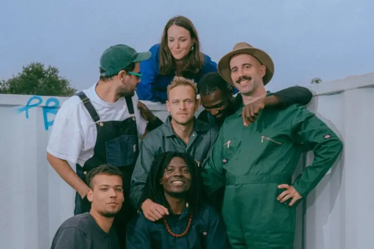 Jembaa Groove seven-piece band group photo outdoors, vocalist Eric Owusu front-center with red beaded necklace