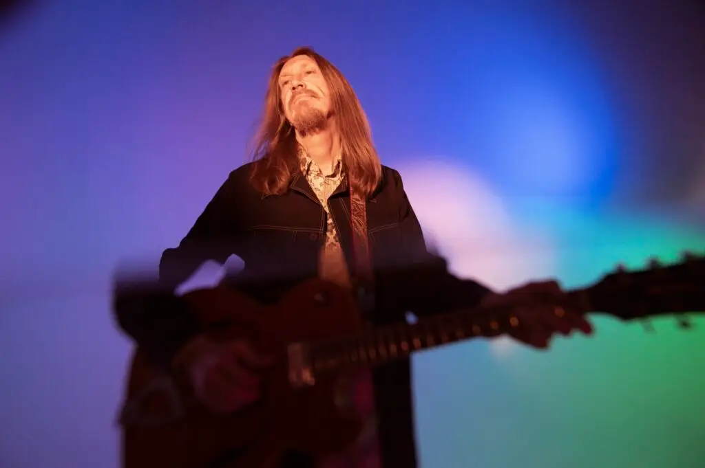 Oliver Wood plays guitar during a press photo session, colorful studio lighting