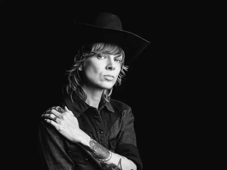 River Shook in a B&W studio press photo, wide-brim black cowboy hat, western shirt, arm tattoos