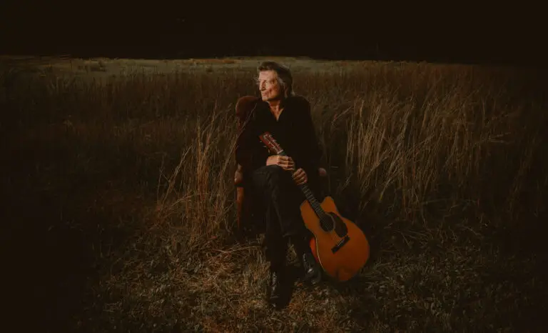 Chris Smither seated in a field with acoustic guitar, Caffe Lena, Saratoga Springs