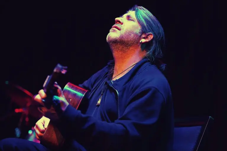 Stéphane Wrembel performing live on Gypsy jazz guitar, head tilted back in expression, dramatic blue and red stage lighting