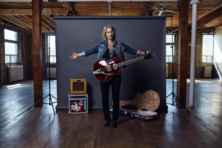 Lynne Hanson holding guitar with arms outstretched in loft studio press photo
