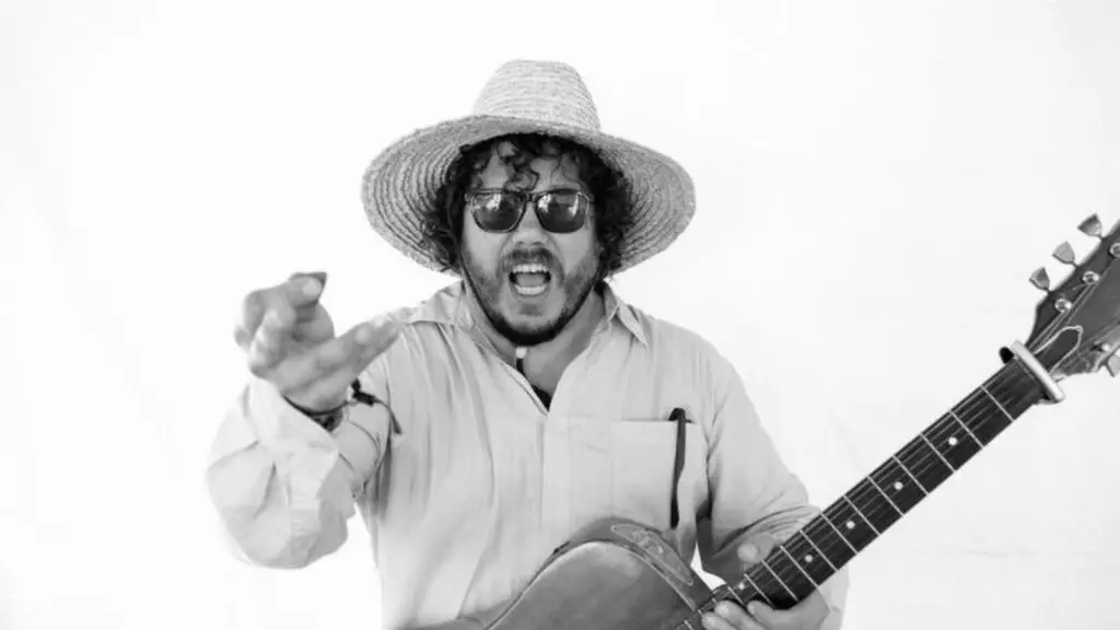 Bobby Bare Jr. with acoustic guitar, energetic performer pose, straw hat and sunglasses