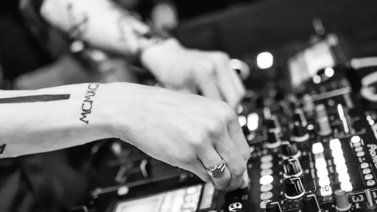 DJ hands on Pioneer mixer at a dance party, tattooed forearm, B&W close-up