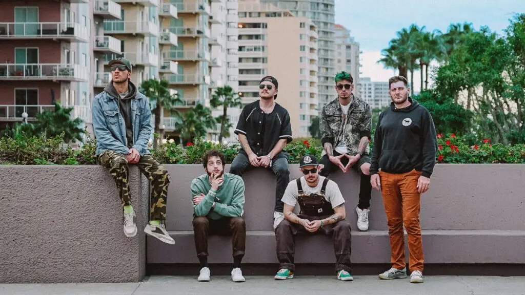 Tropidelic six-piece band poses for a press photo at a tropical outdoor location with palm trees and city skyline