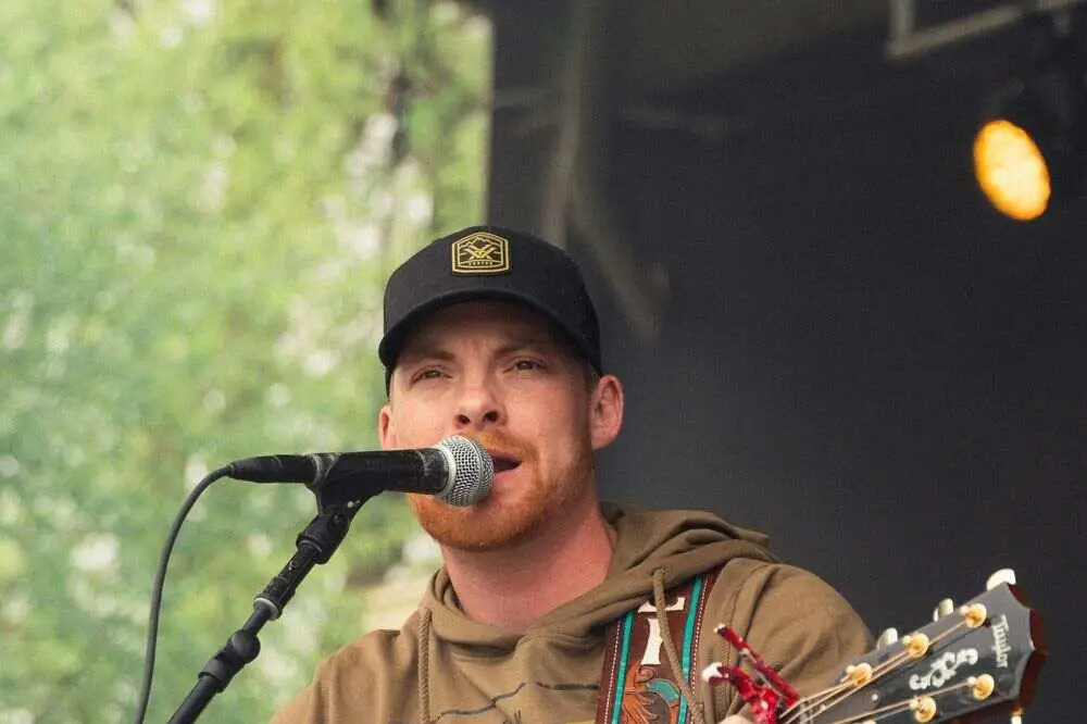 Steven Cali performs live at an outdoor stage, singing into mic while playing acoustic guitar