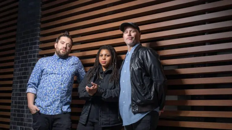 The Nth Power — Nikki Glaspie, Nick Cassarino, and Nate Edgar stand in front of a wood-slat wall