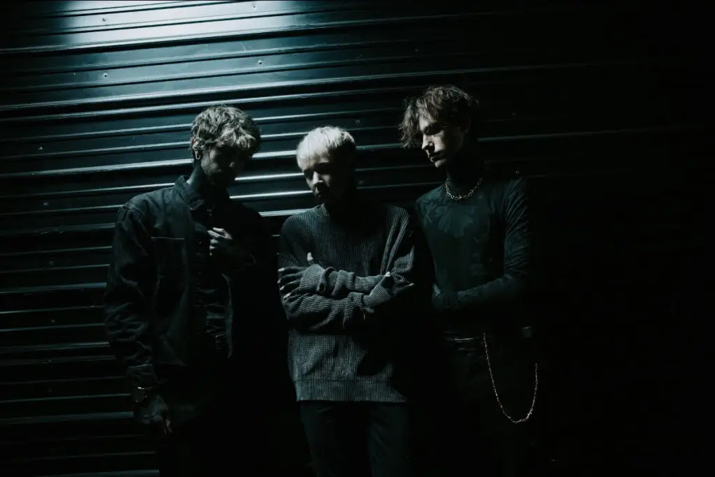 Glasswaves trio posed against corrugated metal backdrop in dramatic dark lighting