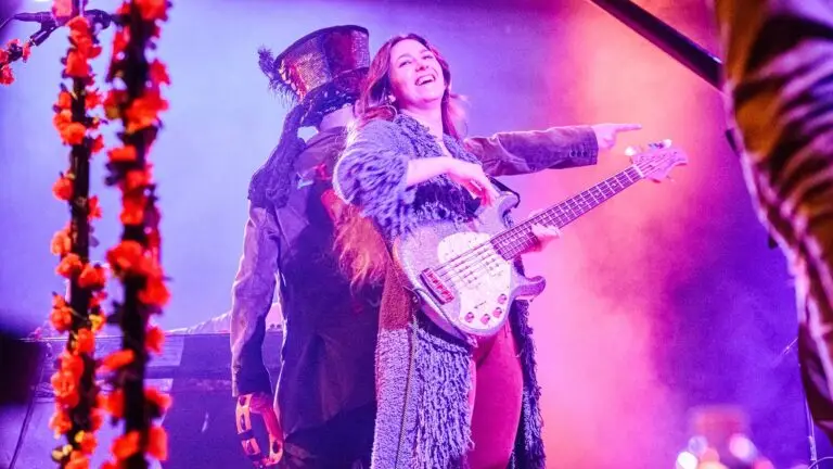 Bearly Dead performs live — bassist Sarah Elaz on stage with rose garland curtains and purple theatrical lighting