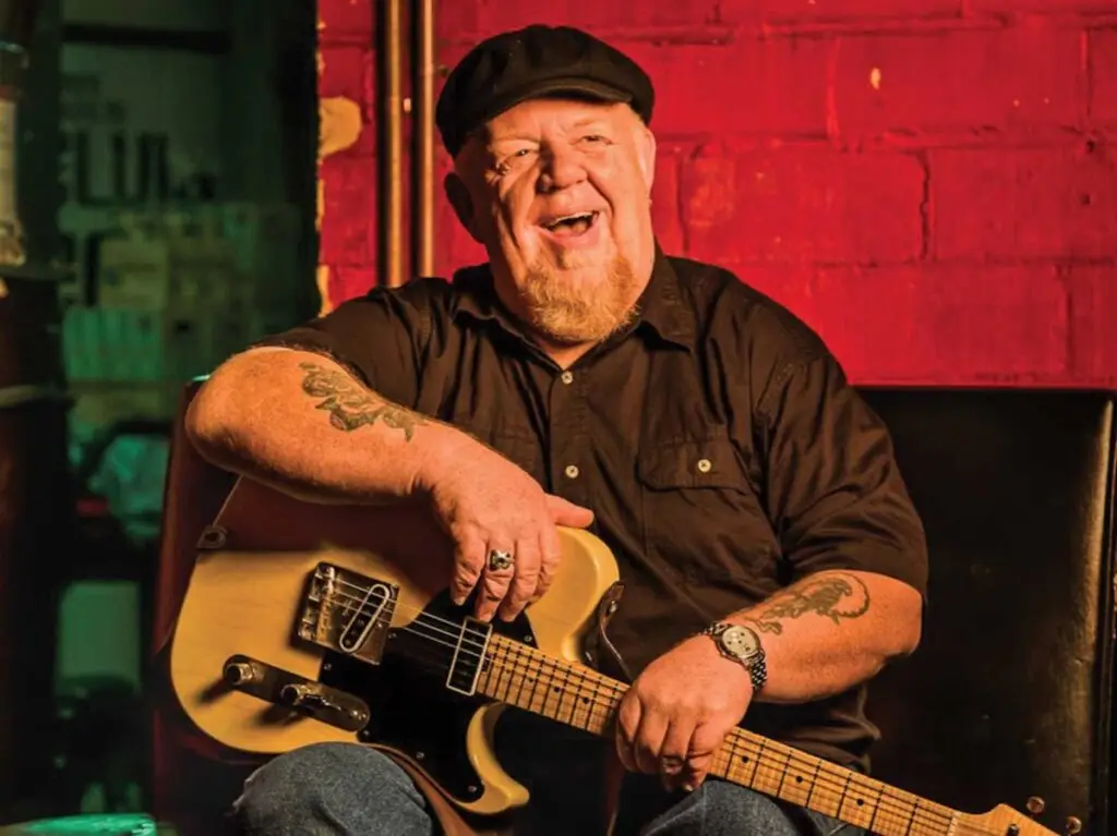 Redd Volkaert laughing with a blonde Telecaster guitar at a music venue