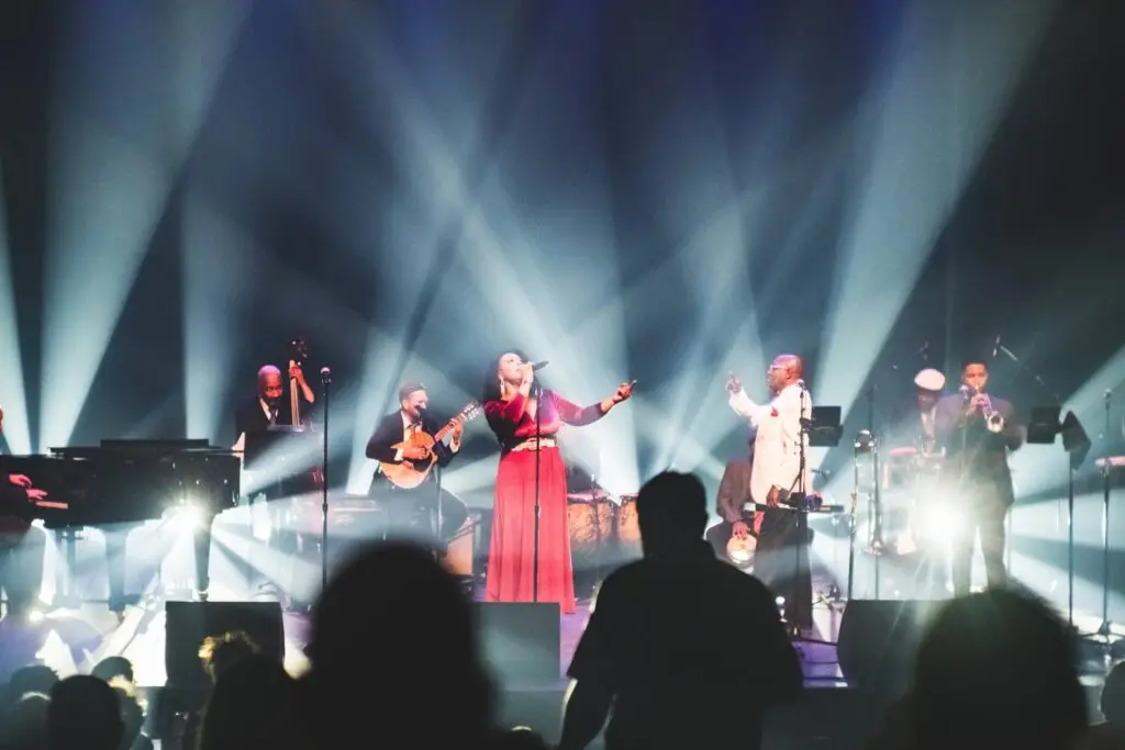 The Buena Vista Orchestra performing live, female vocalist in red dress singing center stage with full ensemble