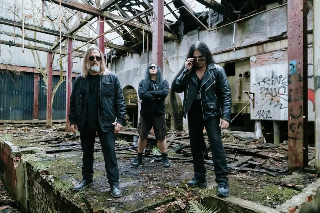 Carnivore A.D. poses in an abandoned industrial ruin, leather jackets and sunglasses, NYC metal trio