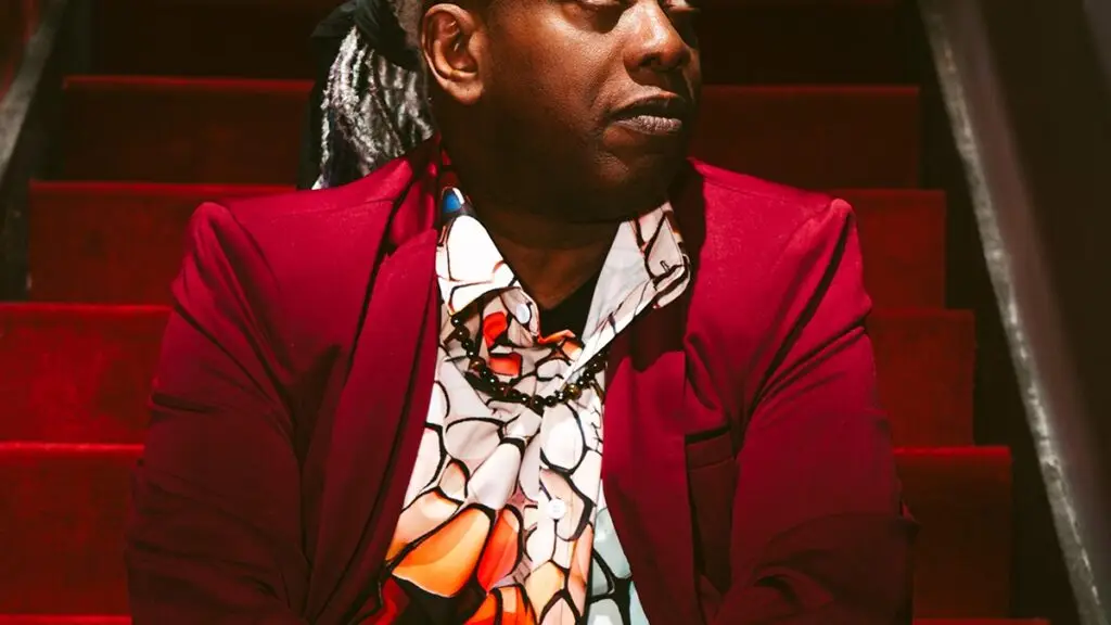 Corey Glover of Living Colour in red blazer on red stairs, The Soul Experience press photo