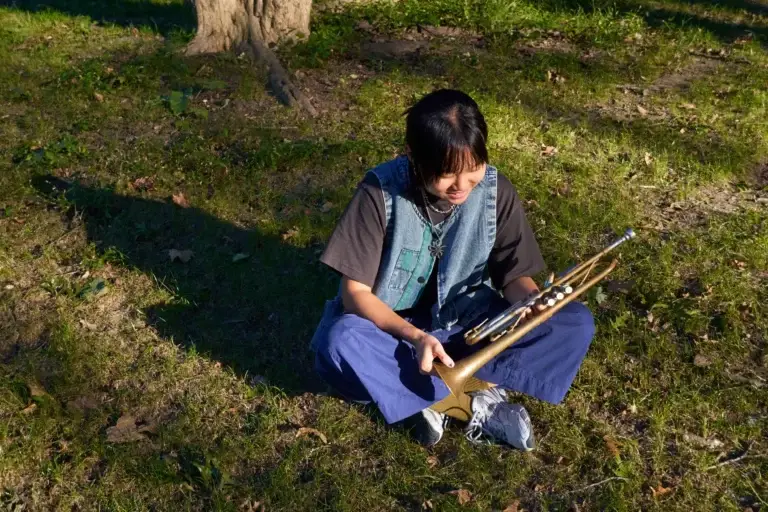 Skylar Tang seated on grass holding her trumpet in an outdoor park setting