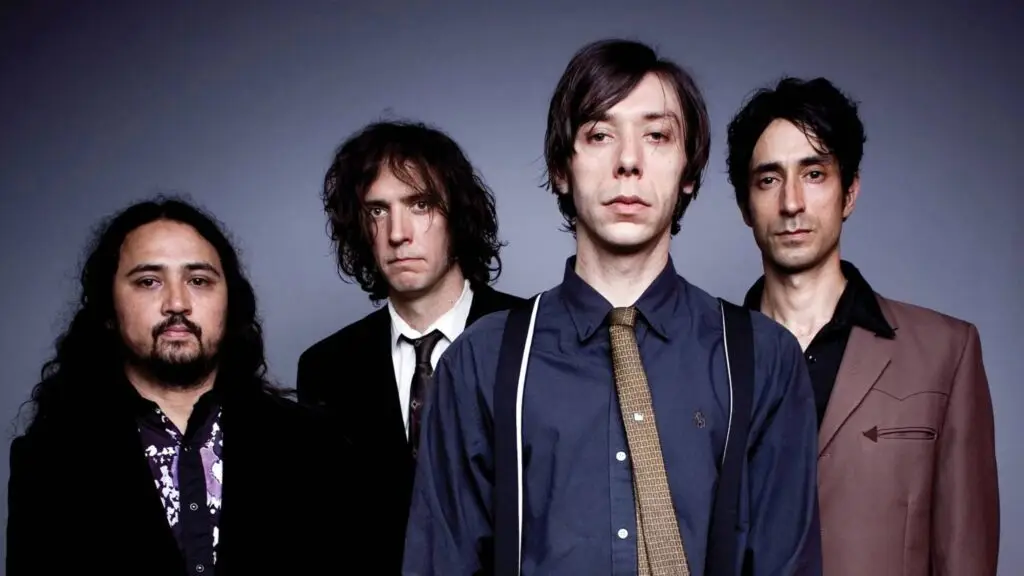 The Sadies band press photo, four members in dark suits and shirts against gray studio background