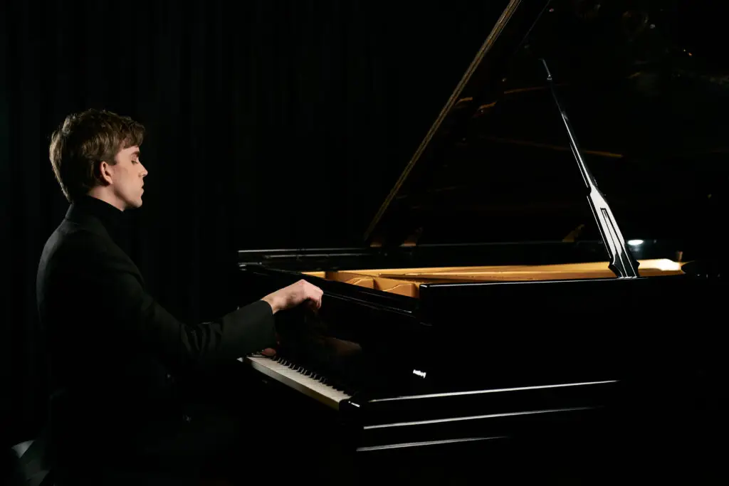 Reed Tetzloff performs at grand piano, profile view with dramatic studio lighting
