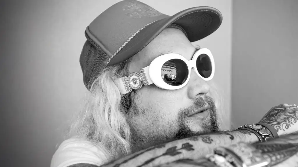 Mihali Savoulidis press photo, white round sunglasses and trucker cap, blond hair