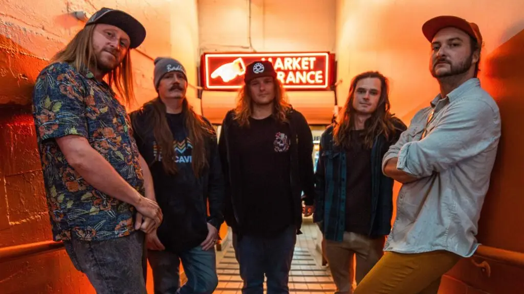 Kash'd Out five-piece band promo photo in orange corridor with neon market entrance sign