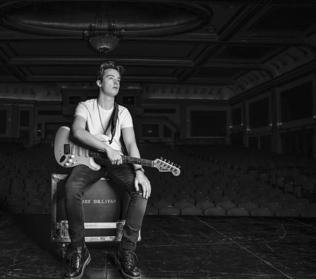 Quinn Sullivan with Fender Stratocaster on stage in empty concert hall, official press photo