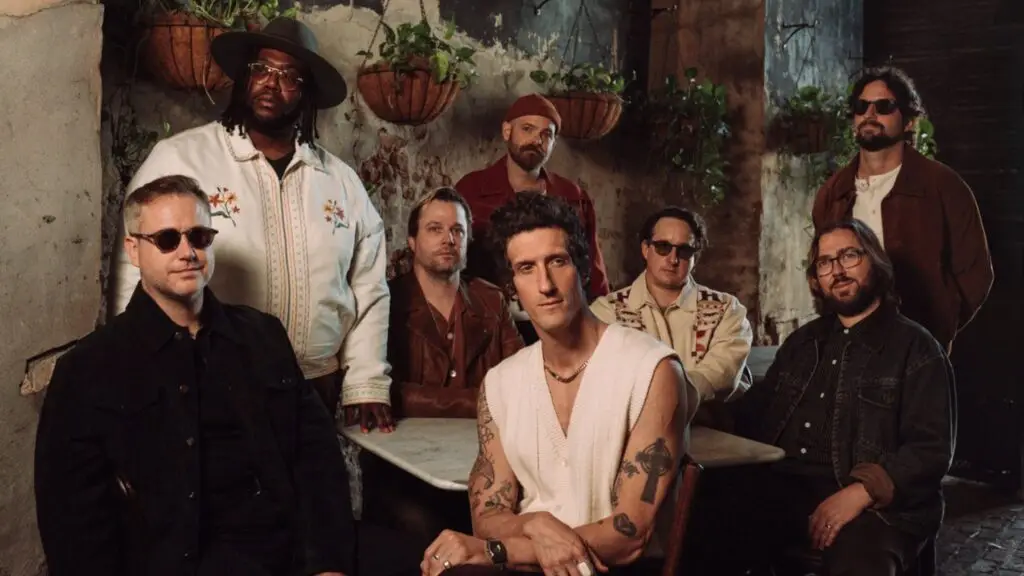 The Revivalists eight-piece band press photo in a rustic New Orleans courtyard, frontman David Shaw centered