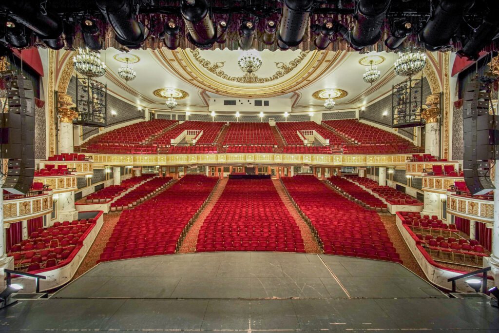 The restored MainStage auditorium at Proctors in Schenectady, seen from the stage — rows of red velvet seats, gilded balconies, and chandeliers