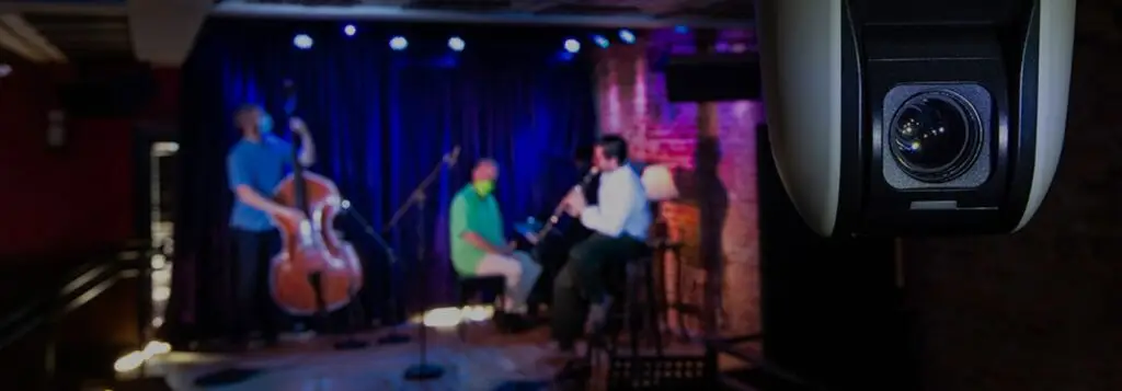 Musicians performing on the Caffè Lena stage in Saratoga Springs, with a livestream camera in the foreground