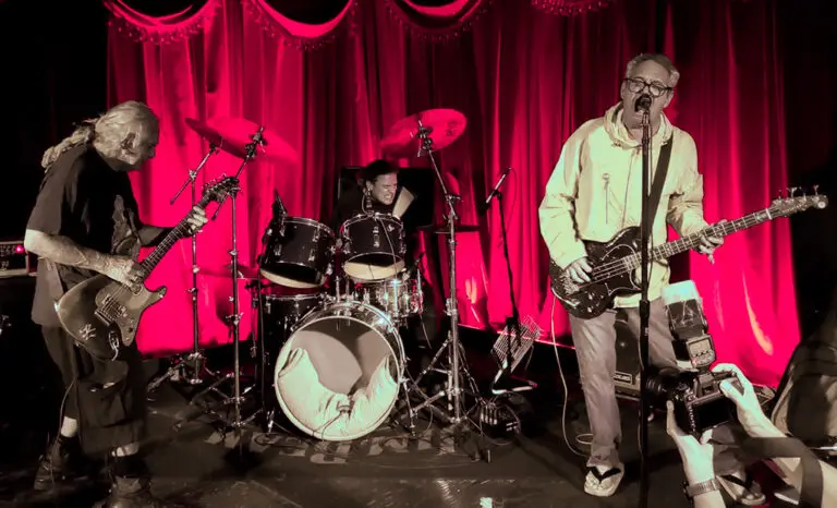 Flipper performing live, guitarist and vocalist on stage with red curtains, intimate punk venue