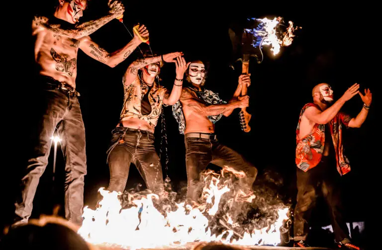 Daikaiju masked members performing live amid open flames, one holding a flaming guitar aloft
