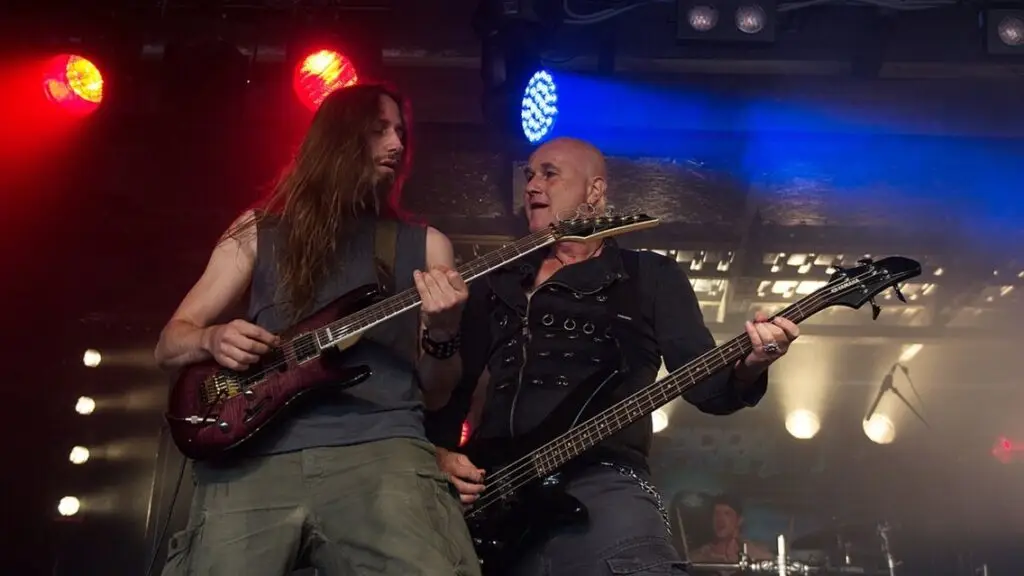 Warrant performing live in concert, two guitarists mid-performance on stage under red and blue lights