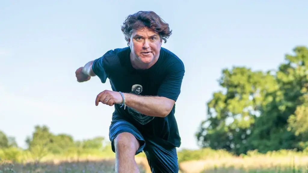 Keller Williams leaping in a sunlit wildflower field, official press photo