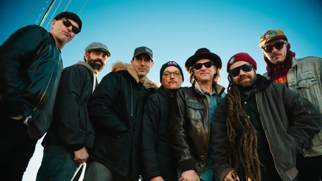 John Brown's Body seven-piece roots reggae band, outdoor group press photo against blue sky