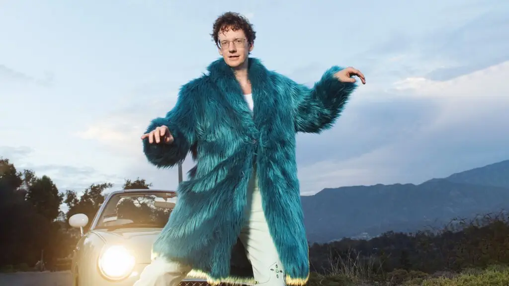 Chris Fleming performing live in an oversized teal faux-fur coat in front of a convertible car