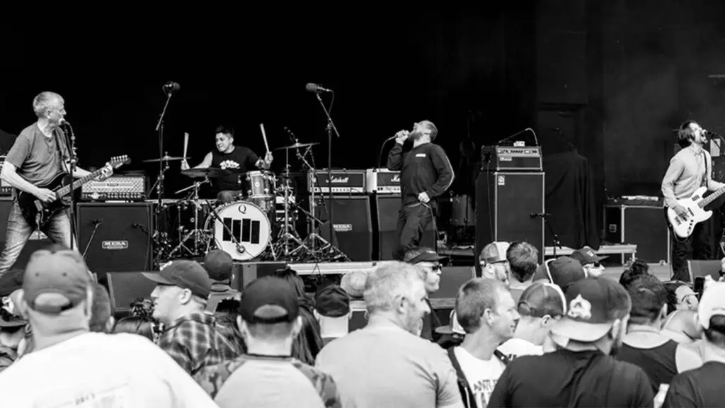 Black Flag performing live on stage, iconic four-bars logo on kick drum, crowd in foreground