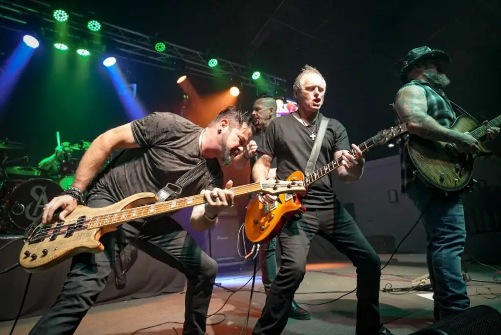 Saving Abel performing live on stage, bassist and guitarists mid-song under green and orange stage lights