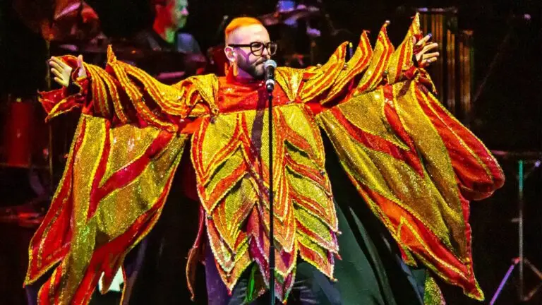 Remember Jones performing live in a dramatic gold and red theatrical costume, arms spread wide at the microphone