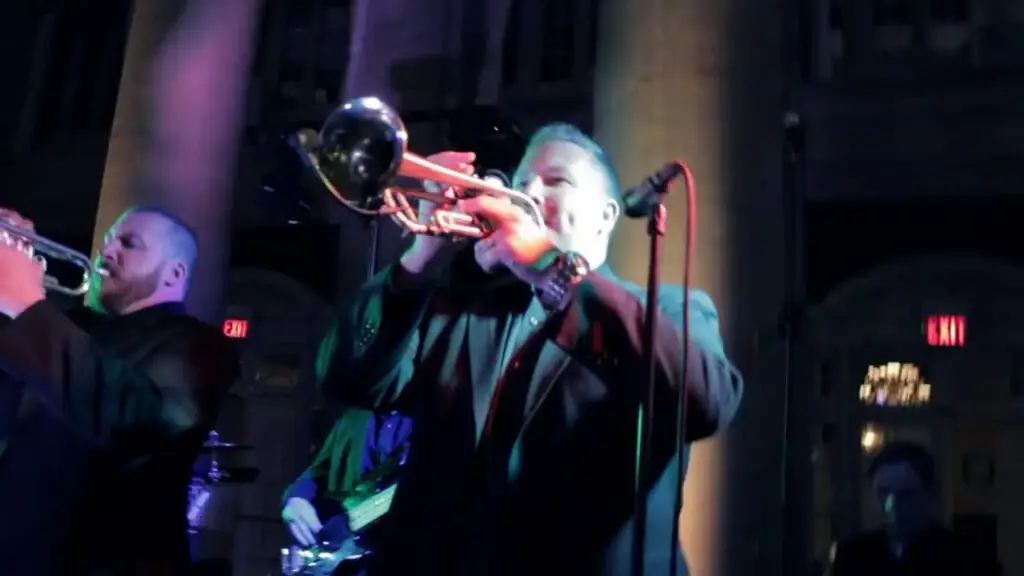 Funk Evolution brass section performing live, two trumpet players mid-song on stage with red and green concert lighting