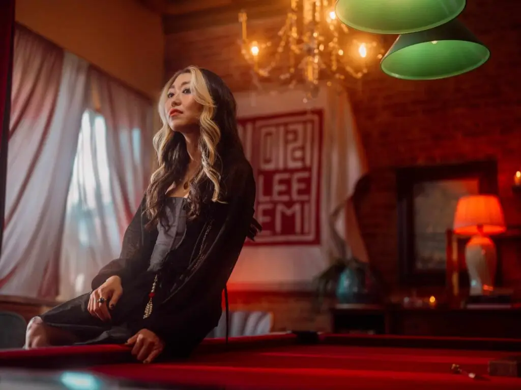 Lee Emi seated on a red billiard table in a moody pool hall, official press photo for DESTROY EVERYTHING
