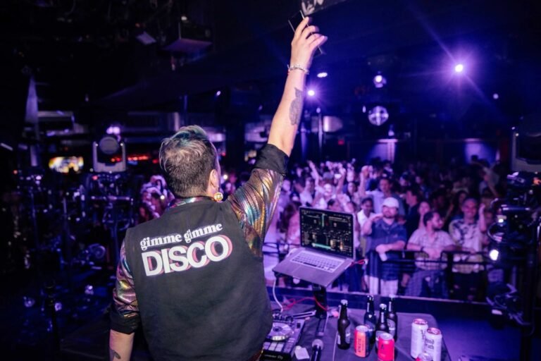 Gimme Gimme Disco DJ performs live at a packed dance party, arm raised over crowd