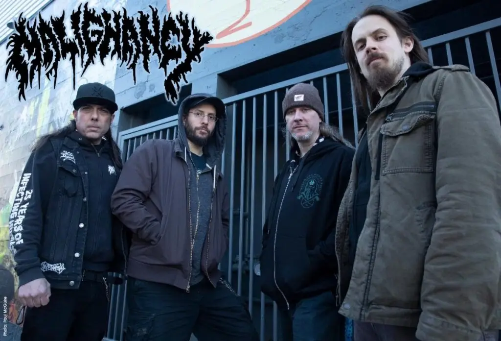 Malignancy band press photo — four members standing outdoors in front of a metal gate