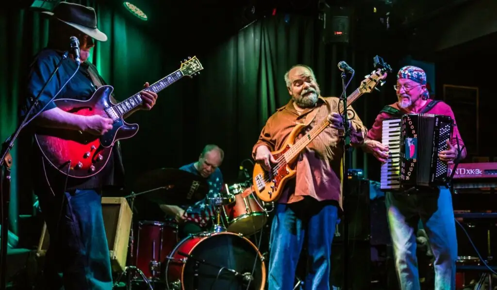 Los Blancos performing live — guitarist, bassist, accordion player, and drummer on a dimly lit club stage