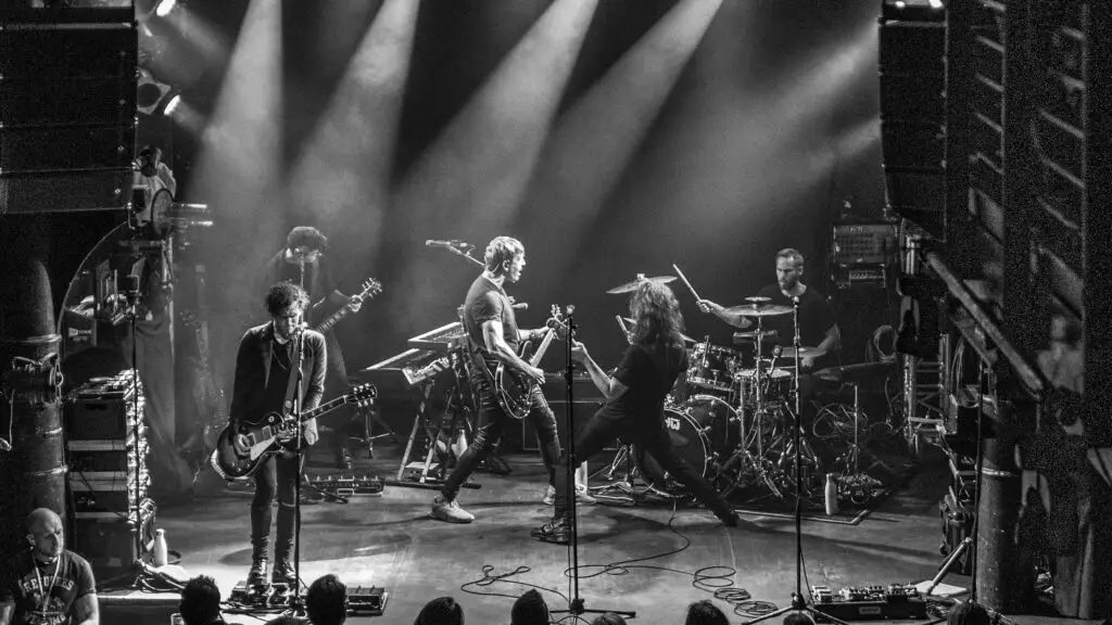 Third Eye Blind performing live on stage, full band with dramatic overhead beam lighting, black-and-white concert photo