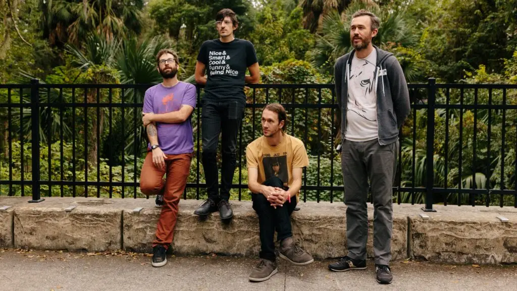 AJJ band members posed outdoors in a botanical garden setting for a press photo