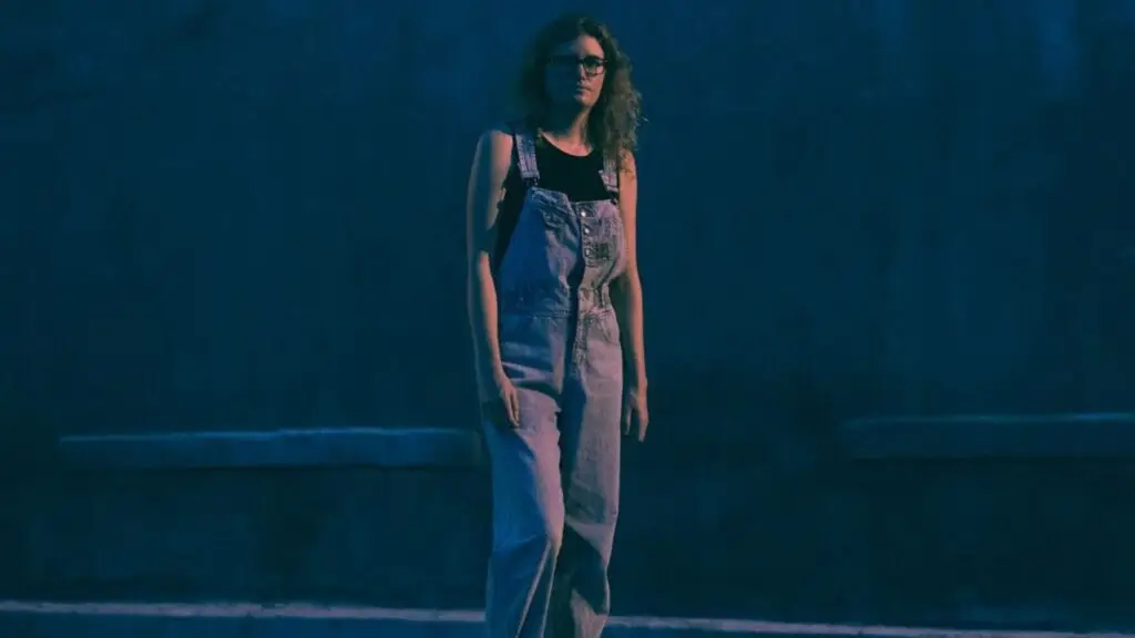 Charlotte Cornfield standing in a blue-lit night setting, denim overalls, promotional photo for her 2026 tour