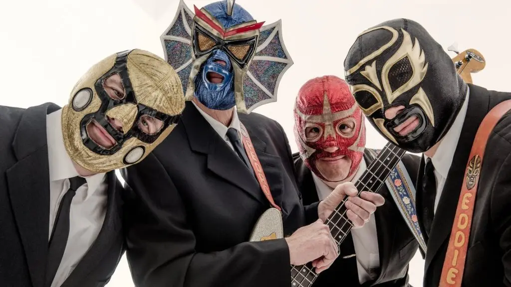 Los Straitjackets in their signature Lucha Libre wrestling masks and suits, holding guitars