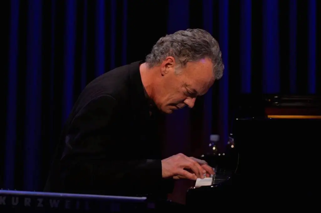 Chuck Lamb performing live at the piano, leaning into the keys under blue stage lighting
