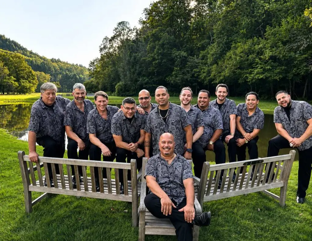 Alex Torres & His Latin Orchestra 12-piece ensemble in matching grey shirts, outdoor press photo by pond